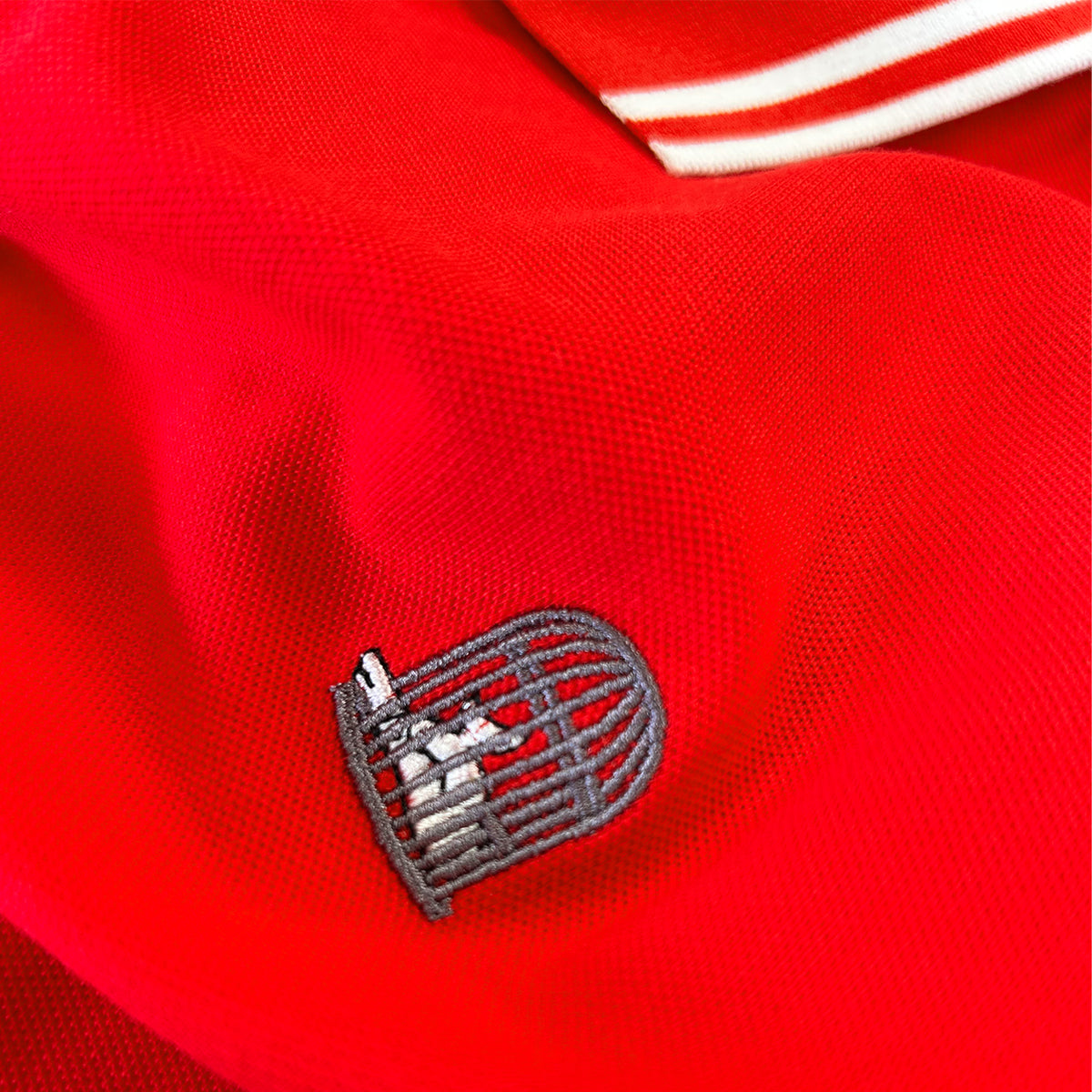 Close-up of the Sauce & Brown birdcage embroidery on the Forza red polo shirt