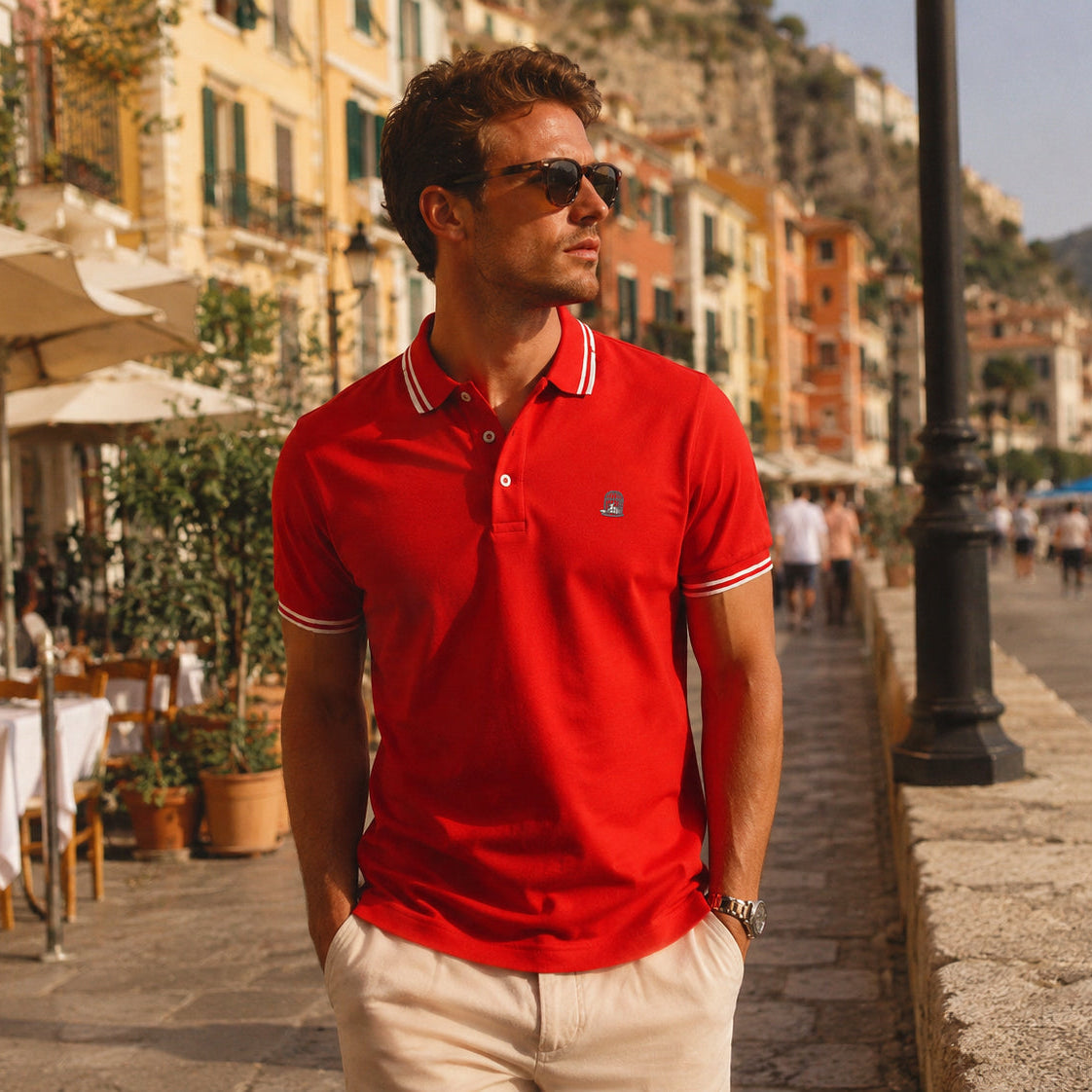 White male model wearing the Sauce & Brown Forza red polo shirt in a Mediterranean coastal town setting