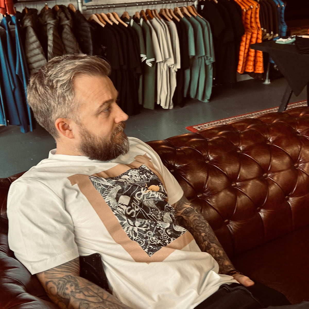 Man sitting on a leather couch in a clothing store with clothes on hangers in the background